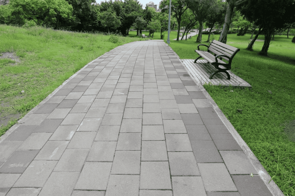 Park walkway paved with rectangular stone tiles and a bench along a green lawn