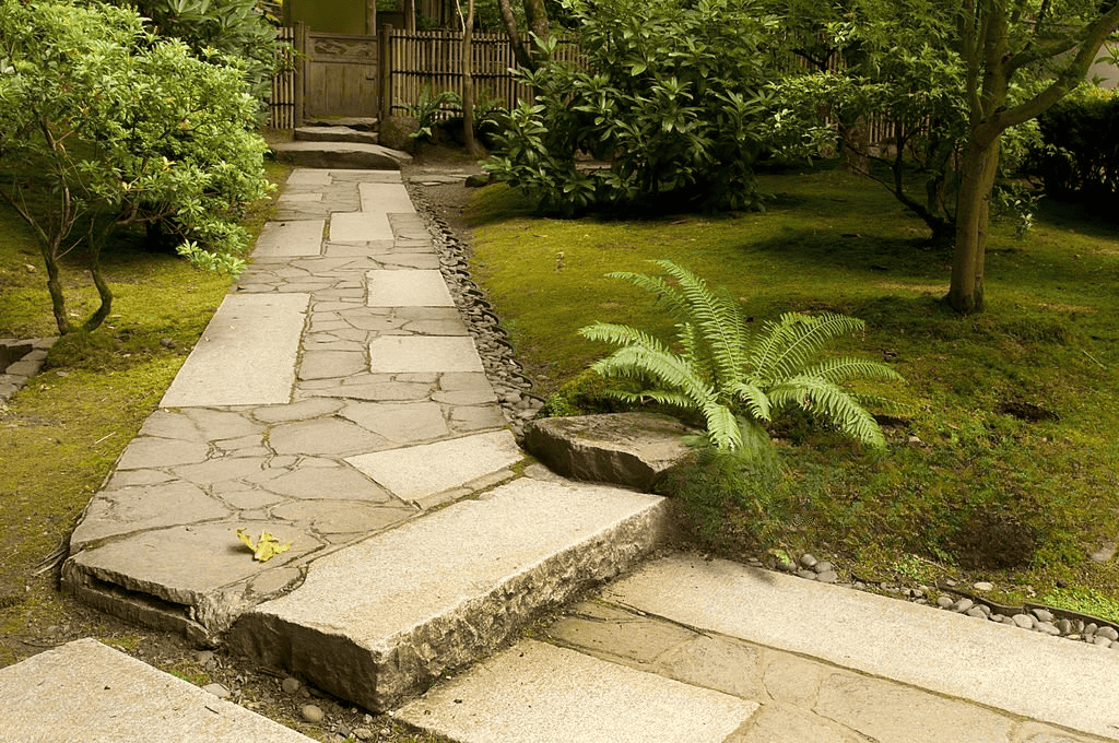 Traditional garden walkway with natural stone paving slabs, moss ground cover, and landscaped outdoor design