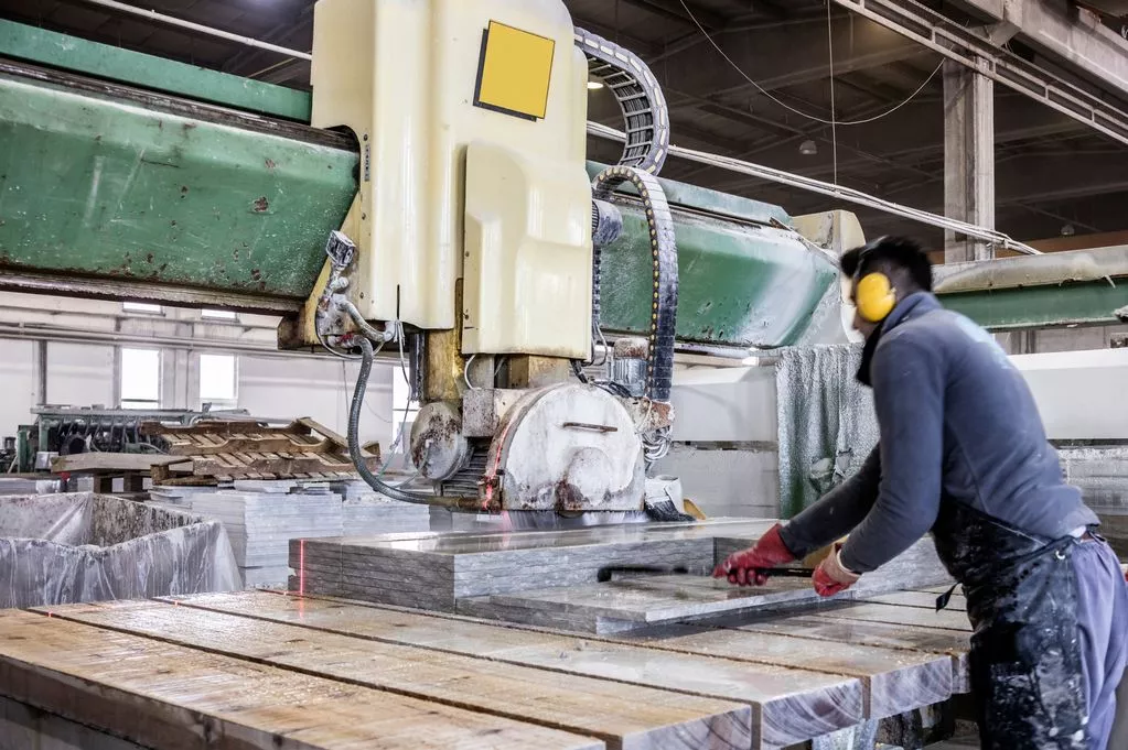 Stone factory worker cutting granite slabs using industrial stone processing machine