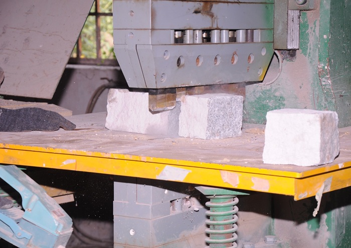 Natural stone cubes being cut by industrial stone processing machine for paving applications