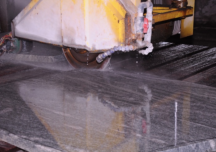Natural granite slab being cut by industrial stone processing machine for flooring and cladding